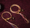 Colorful braided string bracelets with gold charms and tassels on a dark red background