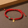 Close up of a wrist wearing a red string bracelet with a small green jade bead and gold charm