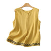 Yellow sleeveless linen tank top with black geometric embroidery on the hem hanging on a wooden hanger