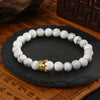 Gold-tone crown charm on a white howlite beaded bracelet displayed on a wooden surface