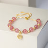 Pink strawberry quartz beaded bracelet with a round gold tone Fu charm on a white surface