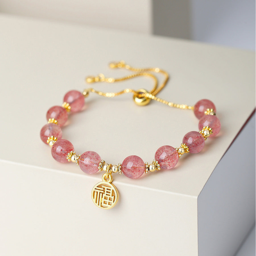 Pink strawberry quartz beaded bracelet with a round gold tone Fu charm on a white surface