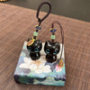 Two small wooden cat charms with blue eyes on a lotus patterned box
