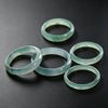 Several translucent light blue green jade rings arranged on a dark surface
