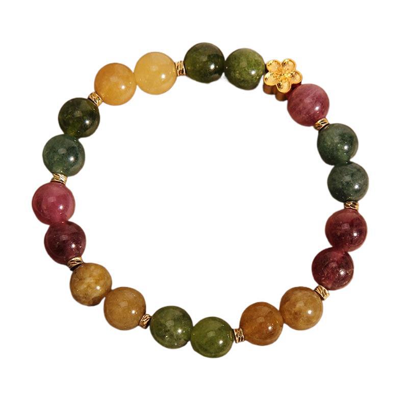 Close up of a beaded bracelet with multi-colored tourmaline stones and a gold flower charm on a white background