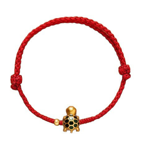 Close-up of a red braided cotton bracelet with a small gold turtle charm on a brown background