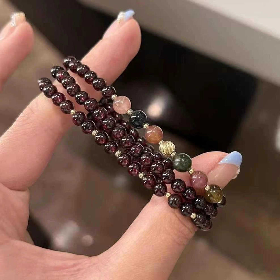 Hand holding a triple strand dark red beaded bracelet with colorful accent stones