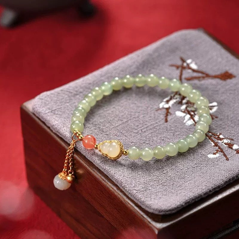 Light green 6mm jade bead bracelet with gold gourd charm on grey box