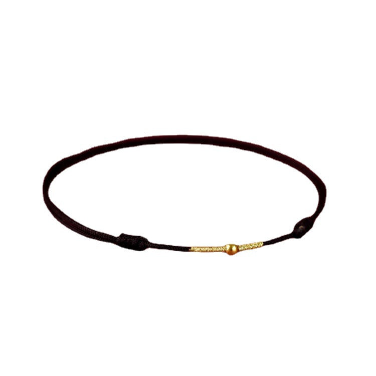 Black braided cord bracelet with a central gold heart-shaped bead on a white background