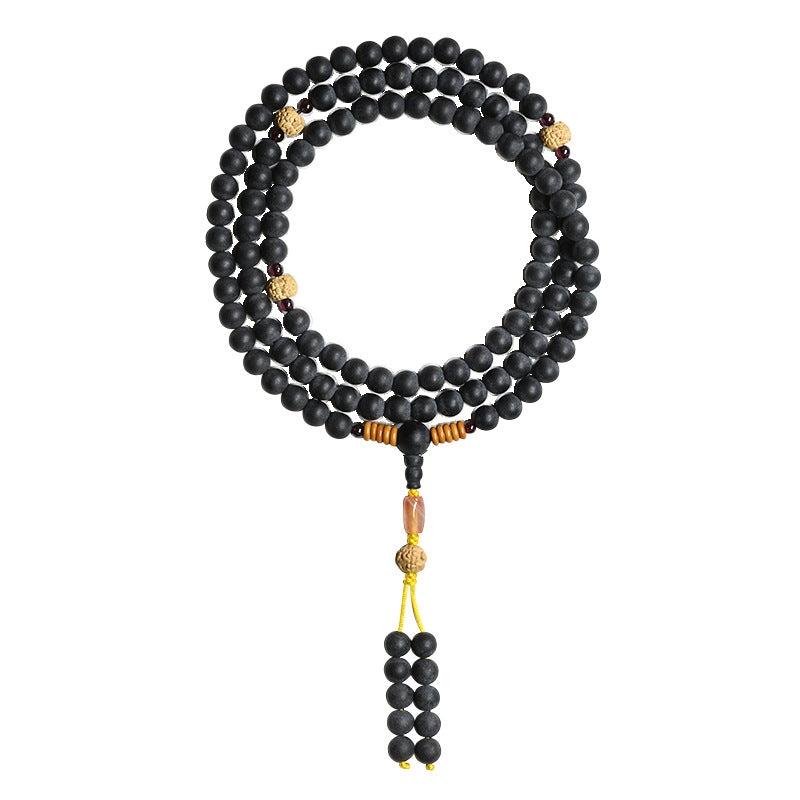 Black medicinal amber mala bracelet wrapped around a wrist with gold accents and a tassel