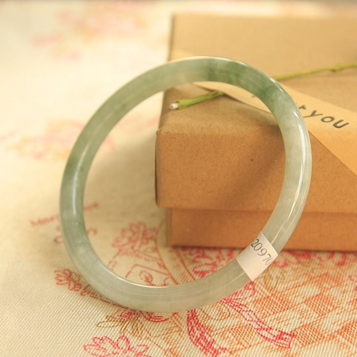 Close up of a light green handmade ice jade bangle bracelet resting on a box