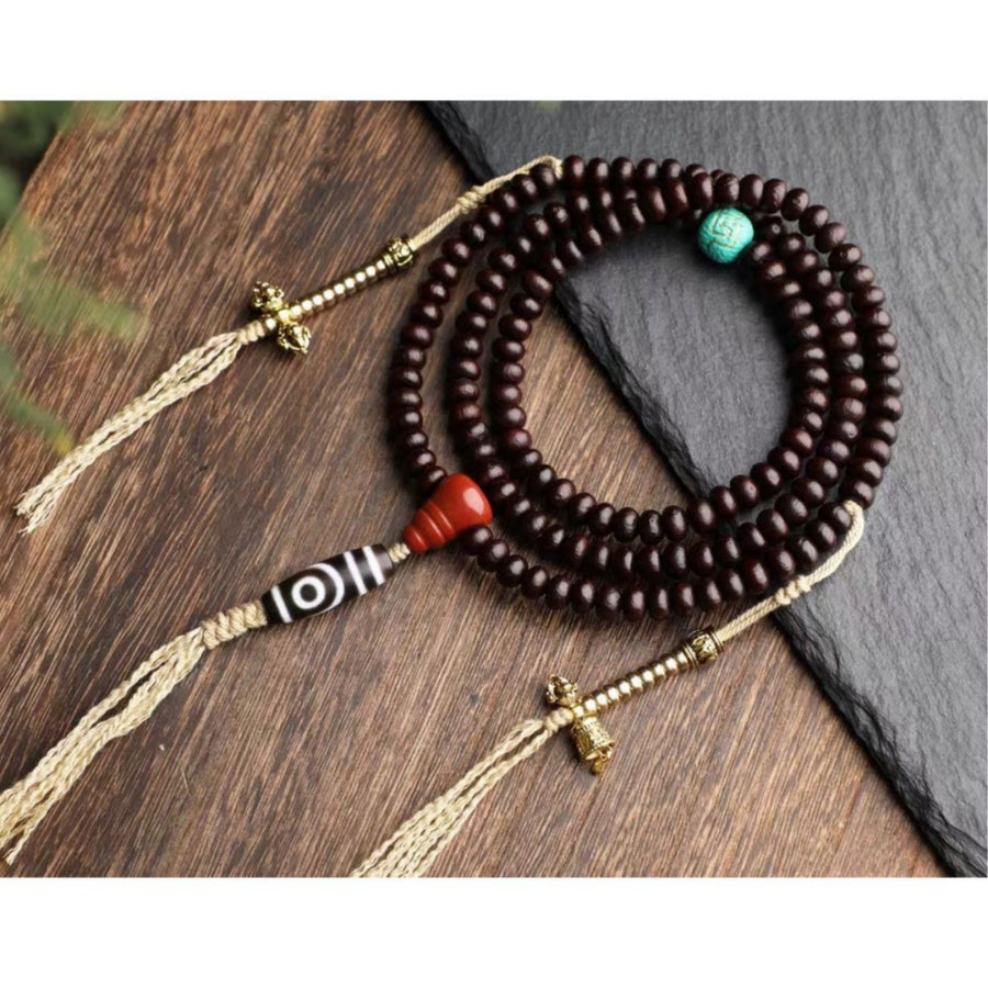 Dark brown bodhi seed mala bracelet with Dzi bead and gold-tone vajra charms on a slate surface