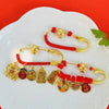 Gold-tone metal safety pin brooch with red cord and lucky charms on a white plate