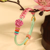 Pink and green braided bracelet with a peach blossom knot hanging from a branch