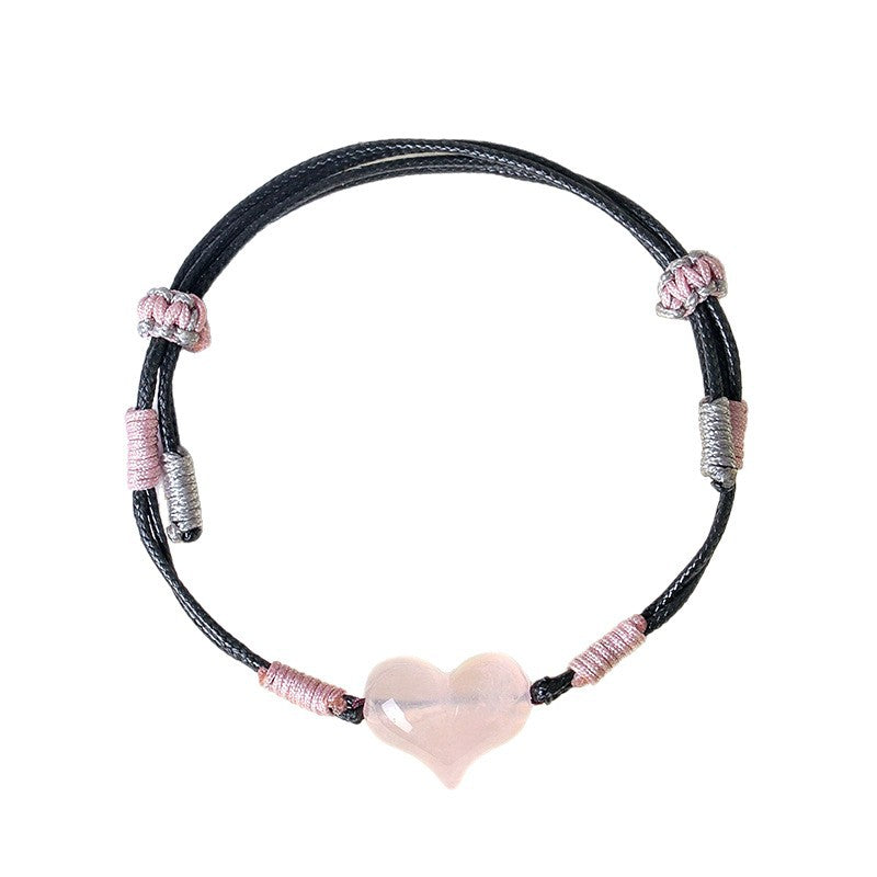 Close up view of a black braided bracelet with a pink rose quartz heart charm