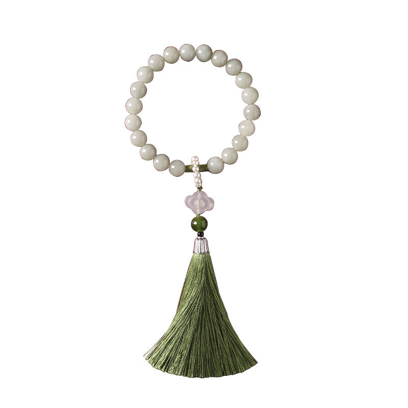 Pale green jade wrist mala with long green tassel resting on an open book