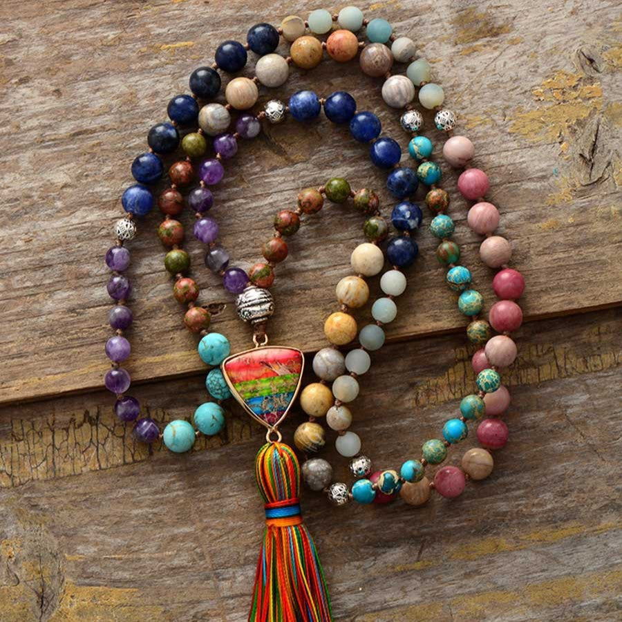 Multi-colored stone mala necklace with a rainbow tassel and triangle pendant on wood