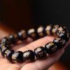 Polished black wooden bracelet with gold script held in hand