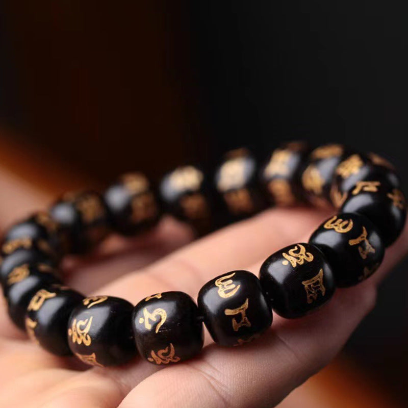 Polished black wooden bracelet with gold script held in hand