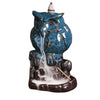 Blue ceramic owl incense burner with white smoke flowing from its beak down a rocky base