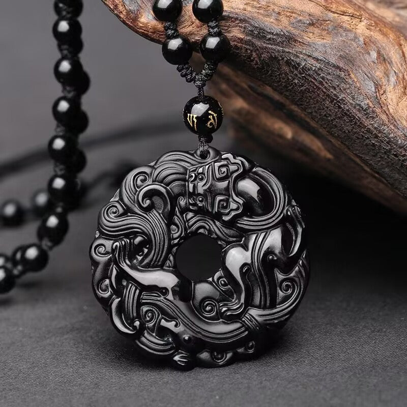 Close up of a carved black obsidian pendant featuring a dragon and pixiu design on a peace buckle shape