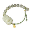 Close up of a white jade bracelet with a carved animal figure and silver charm on a wooden surface