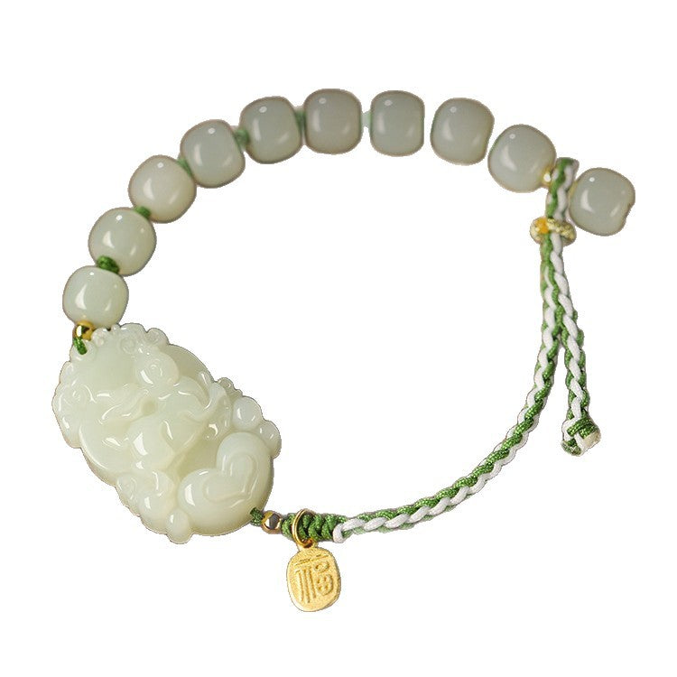Close up of a white jade bracelet with a carved animal figure and silver charm on a wooden surface