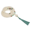 Coiled white Bodhi seed mala bracelet with green accents and tassel on a textured background
