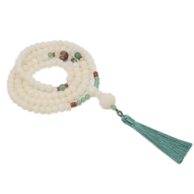 Coiled white Bodhi seed mala bracelet with green accents and tassel on a textured background