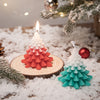 A lit red and white gradient Christmas tree candle on a wooden slice surrounded by snow.