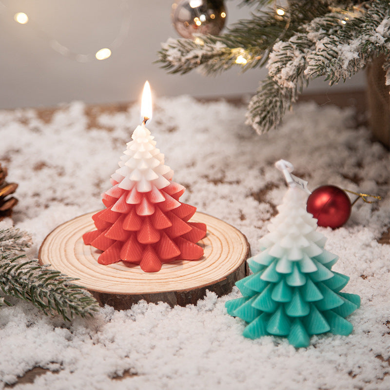 A lit red and white gradient Christmas tree candle on a wooden slice surrounded by snow.