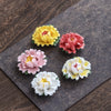 Five colorful ceramic peony flowers arranged on a dark textured mat
