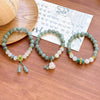 Three styles of green and white jade bracelets with gold charms on a wrist