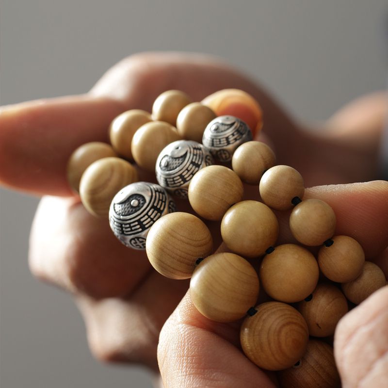 Hand holding a peach wood bracelet with silver Bagua beads