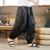 A man wearing black loose-fitting harem pants with a subtle dragon pattern.