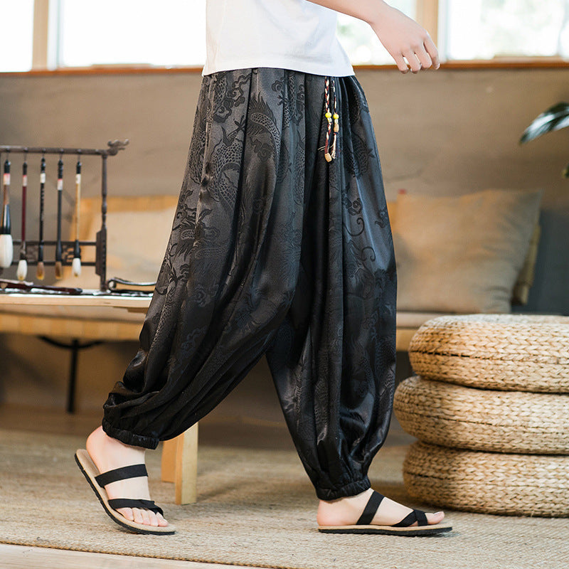 A man wearing black loose-fitting harem pants with a subtle dragon pattern.