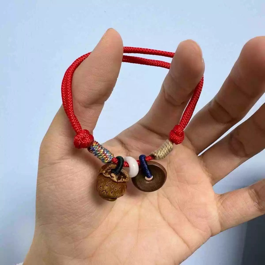 Close-up of a red braided bracelet with a peach wood charm and coin held in a hand