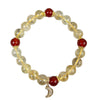 Close-up of a yellow citrine beaded bracelet with red accent beads and a small gold crescent moon charm resting on wood