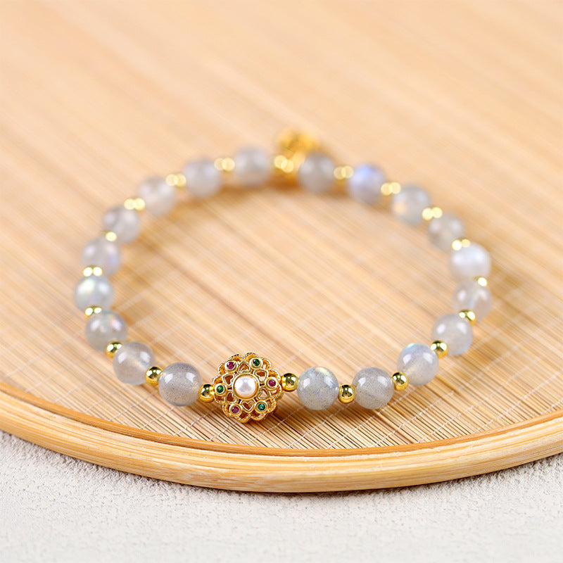 Close-up of a moonstone beaded bracelet with a gold flower charm on a bamboo surface