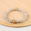 Close-up of a moonstone beaded bracelet with a gold flower charm on a bamboo surface