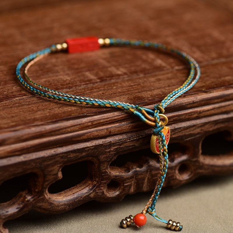 Close-up of a blue and gold braided bracelet with a red rectangular charm on a wooden surface