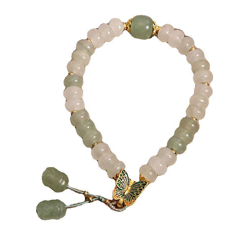 Close up of a bracelet with white and green abacus beads and a gold butterfly charm