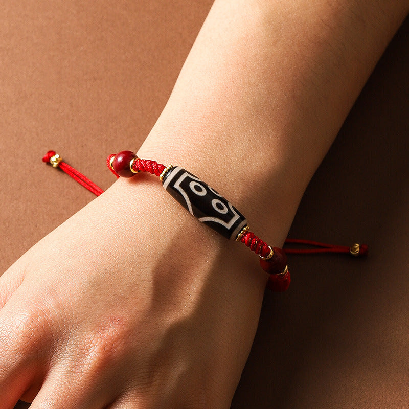 A wrist wearing a red braided cord bracelet with a black and white patterned Dzi bead.