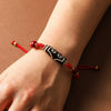 A wrist wearing a red braided cord bracelet with a black and white patterned Dzi bead.