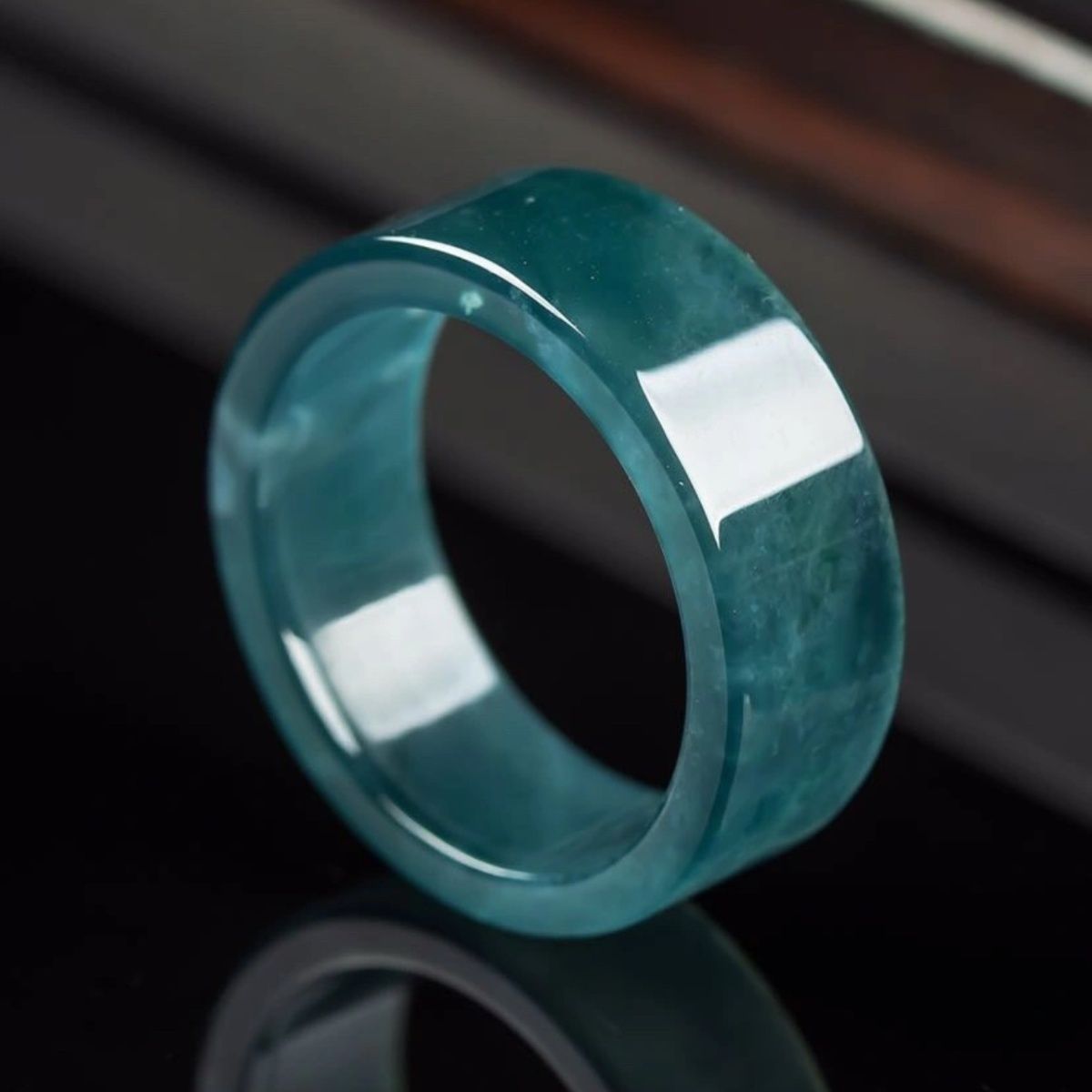 Close up of a smooth blue water jade ring on a dark surface