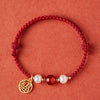 Close-up of a red braided bracelet with a gold charm, white pearls, and a red agate bead.