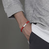 Close-up of a man wearing a red braided bracelet with a silver bar charm on his wrist