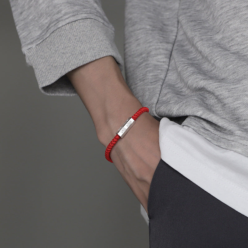 Close-up of a man wearing a red braided bracelet with a silver bar charm on his wrist