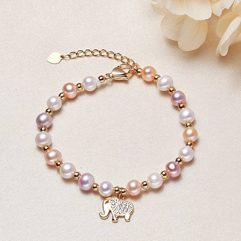 Close up view of a pearl bracelet with a gold elephant charm on a beige background