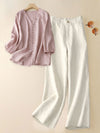 Pink V-neck blouse and white wide leg pants laid flat on a beige background